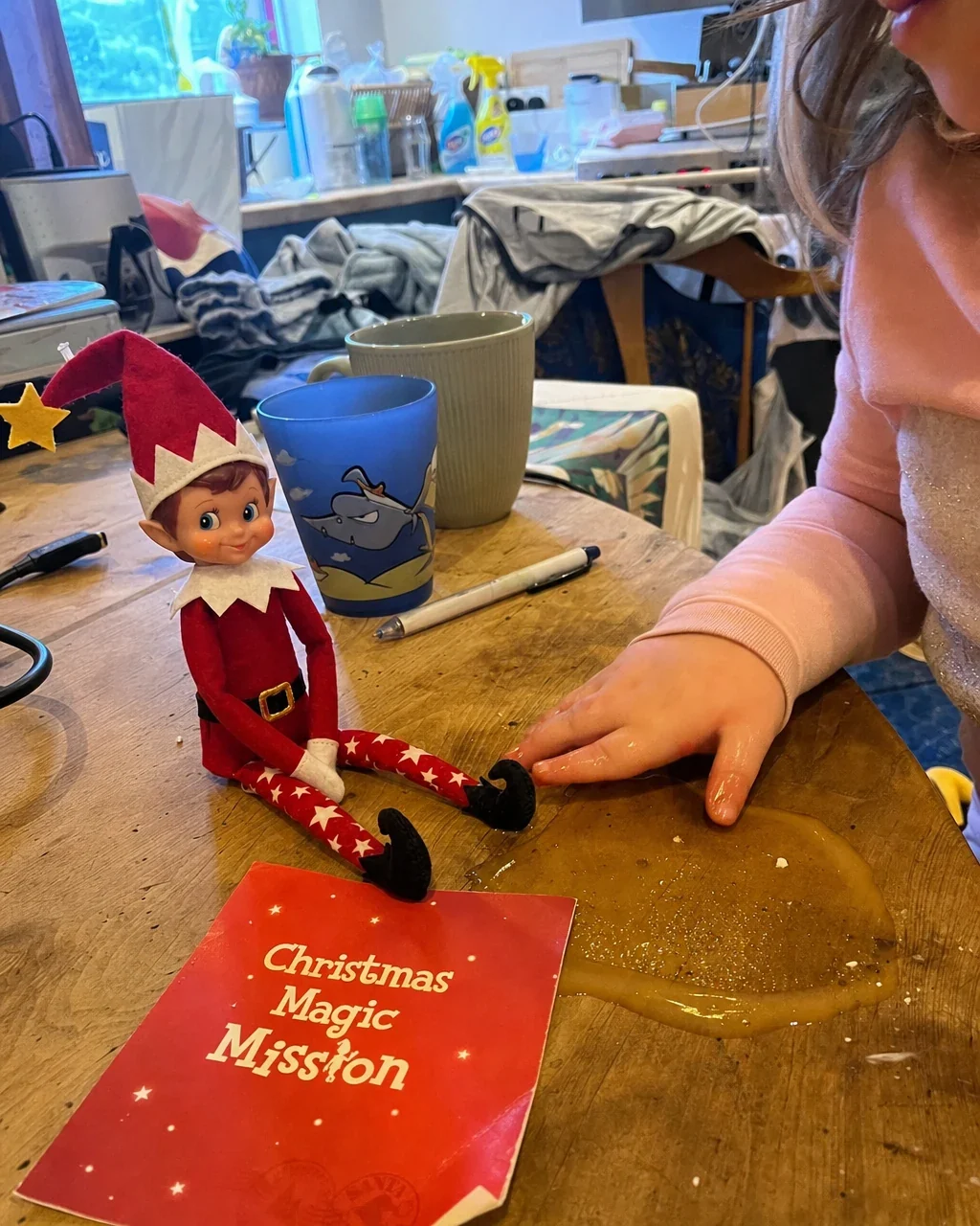 A well-used mission card on a cluttered kitchen table beside a toddler&rsquo;s sticky hand