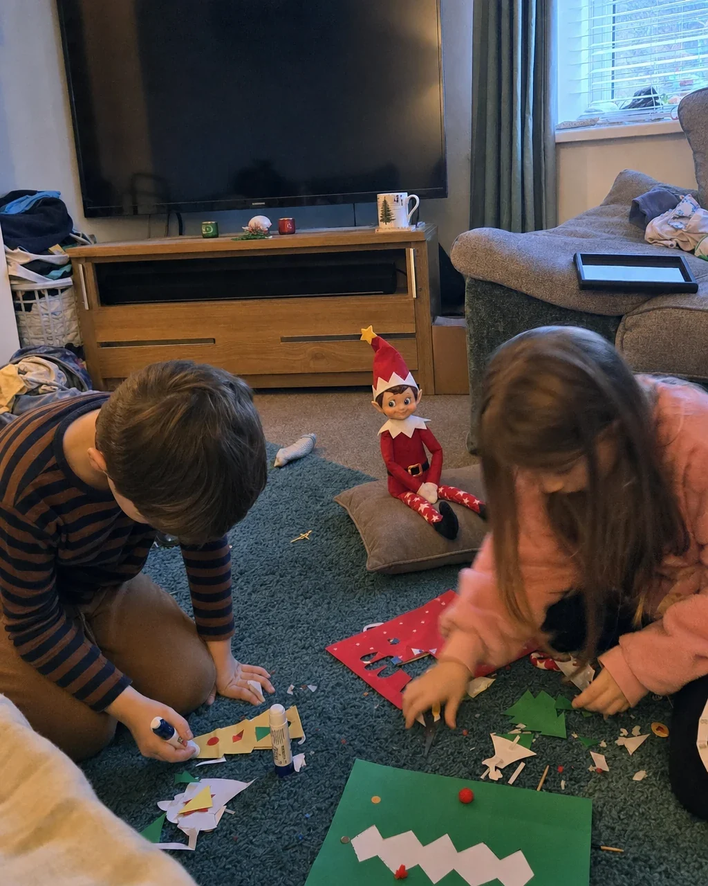 Two children making paper decorations on the rug with the television switched off