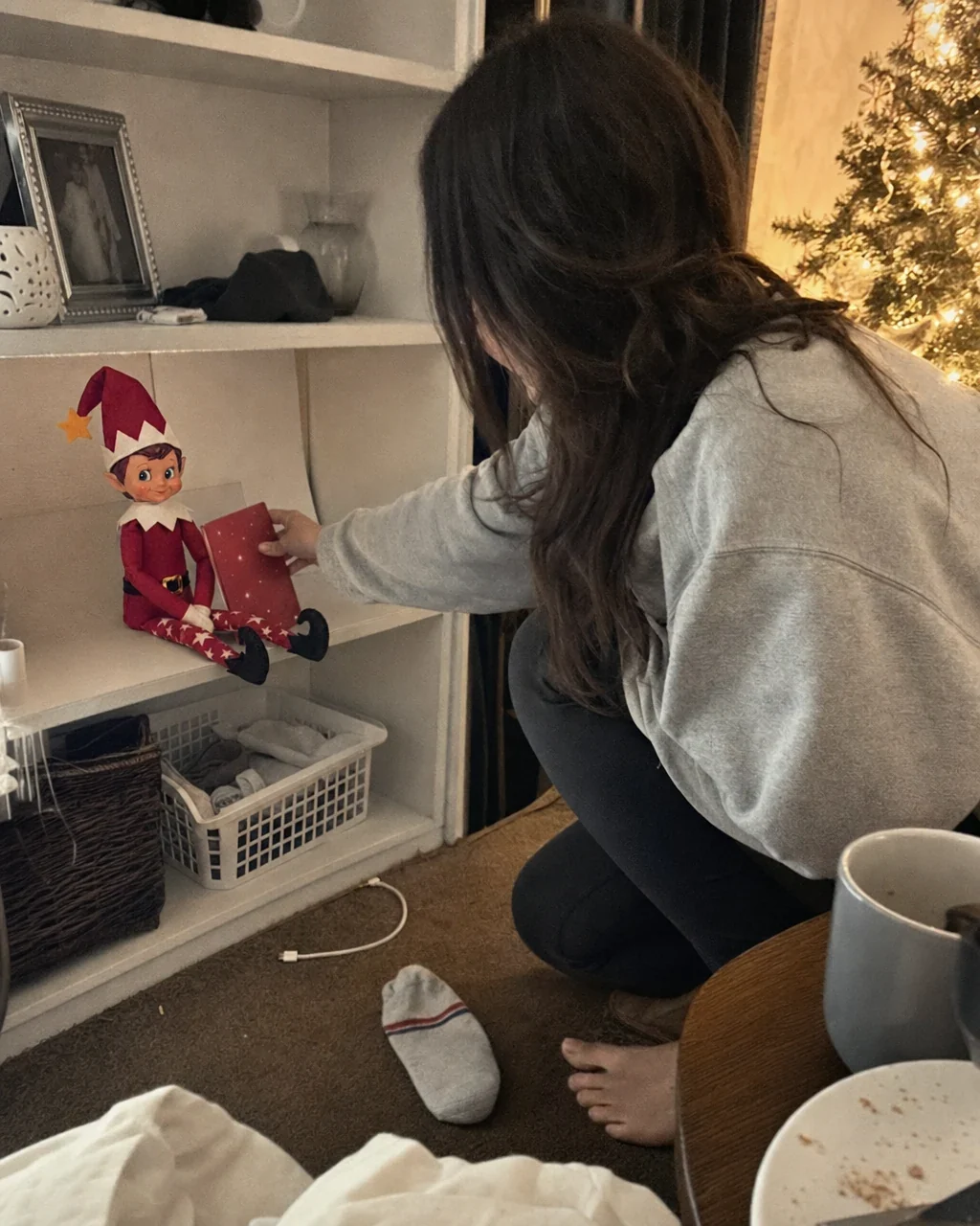 A mother crouching by a shelf at night, propping tomorrow&rsquo;s mission card against Pip