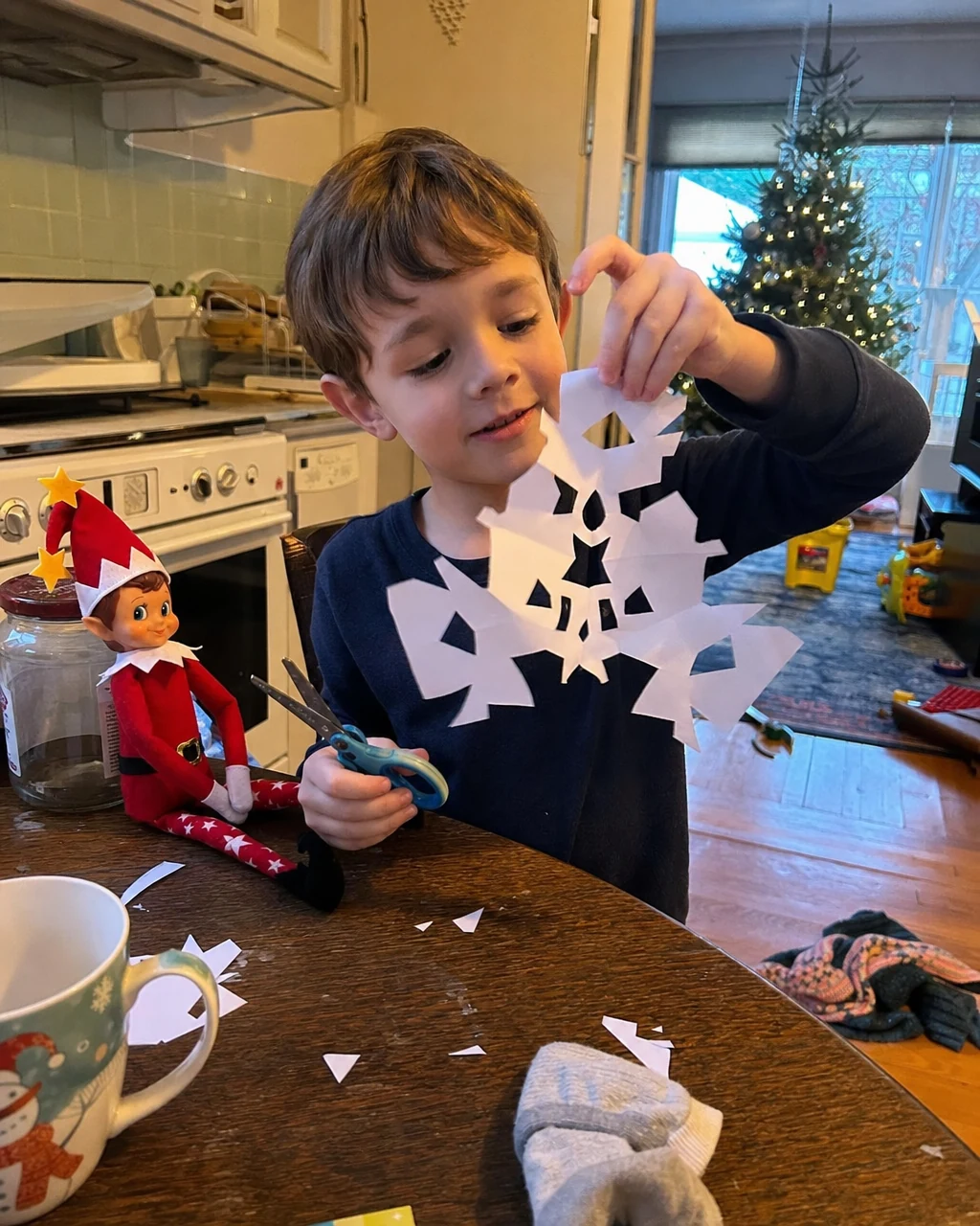A boy holding up a paper snowflake he has just cut out