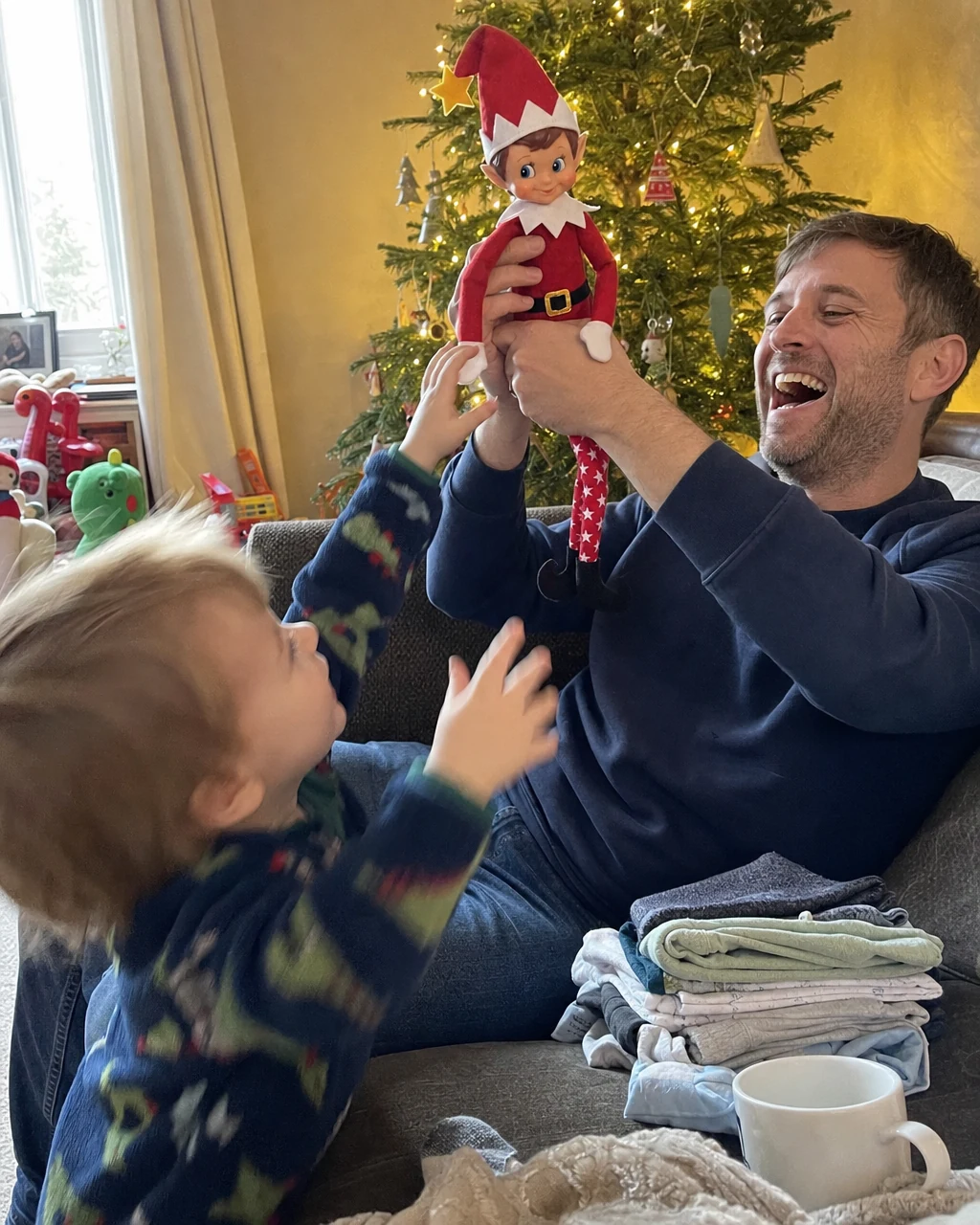 A father holding Pip up in the air while a toddler reaches for him